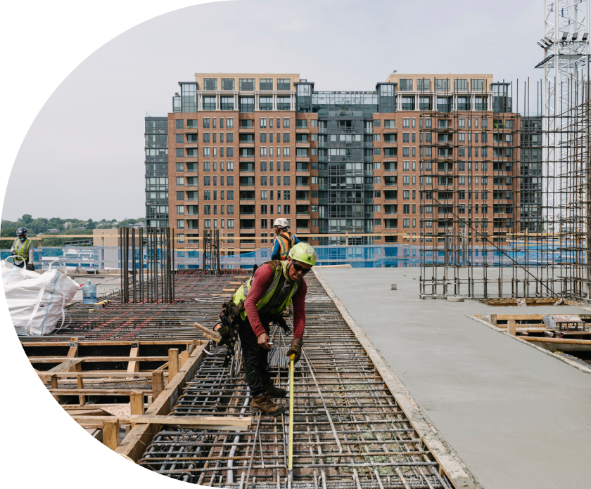 Workers holding a measuring tape atop a building being constructed